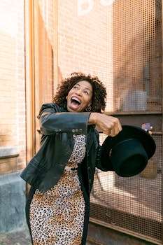 Elderly woman with a vibrant smile holding a black hat, embodying joy and fashion outdoors.