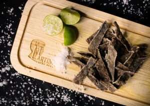 Top view of dried meat strips with lime and sea salt on a rustic wooden board.