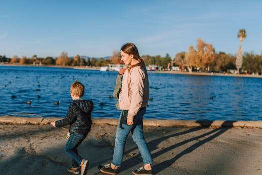 A mother and child walking by a lake on a sunny day, enjoying nature.