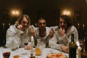Group of three men in medieval attire enjoying a candlelit dinner with wine.