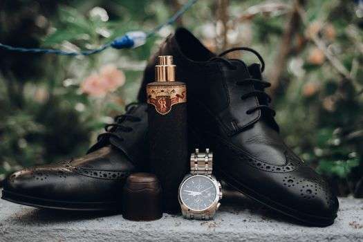 Display of stylish men's accessories including leather shoes, perfume, and a wristwatch outdoors.